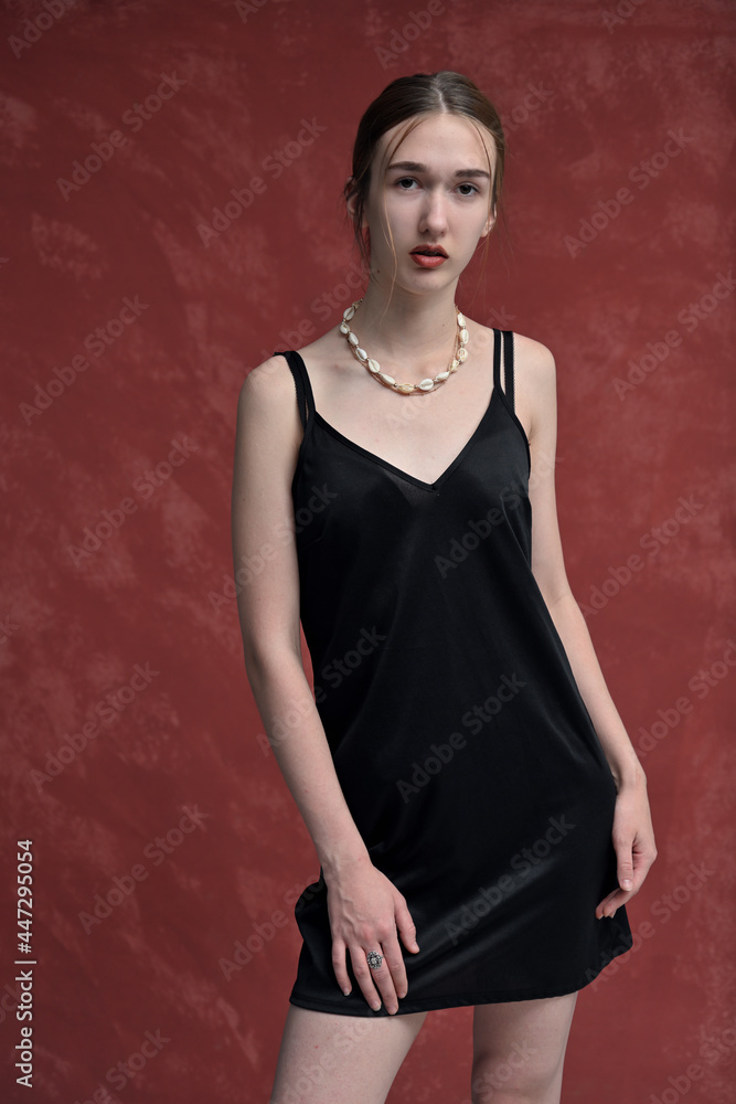 Portrait of a skinny caucasian model in a black dress posing on a red background looking directly at the camera Portrait of a skinny caucasian model in a black dress posing on a red background looking directly at the camera