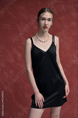 Portrait of a skinny caucasian model in a black dress posing on a red background looking directly at the camera