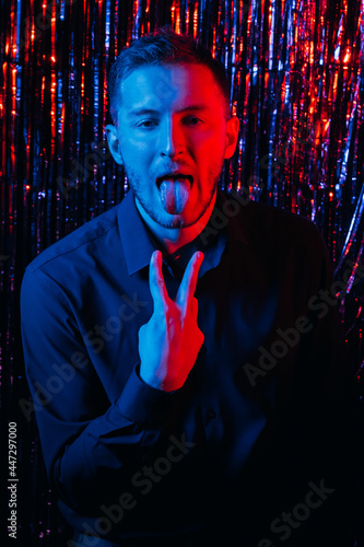 Bad party. Boring celebration. Festive failure. Holiday killjoy. Red blue neon light funny disappointed disgusted drunk man throwing up vomiting gesture on dark shiny tinsel. photo