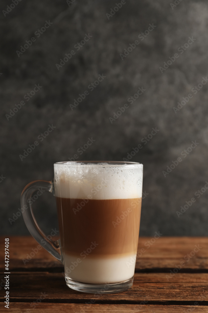 Glass cup of delicious layered coffee on wooden table against grey background, space for text Glass cup of delicious layered coffee on wooden table against grey background, space for text