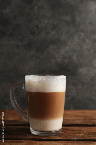 Glass cup of delicious layered coffee on wooden table against grey background, space for text