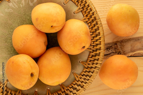 Several organic ripe apricots on a ceramic dish, on a wooden table, close-up, top view.