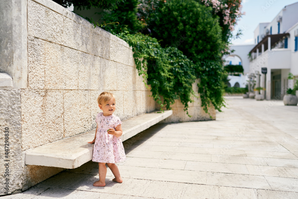 Little girl stands at a bench near a stone wall in the courtyard