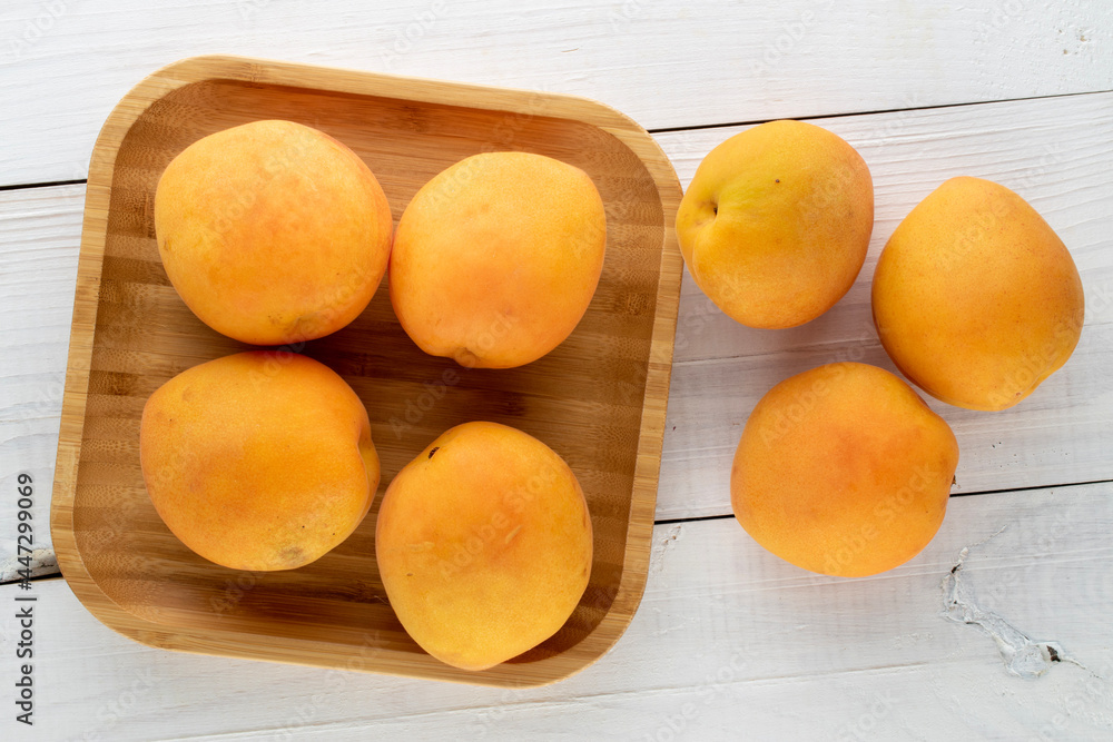 Several organic ripe apricots with a tray of bamboo, on a wooden table, close-up, top view.