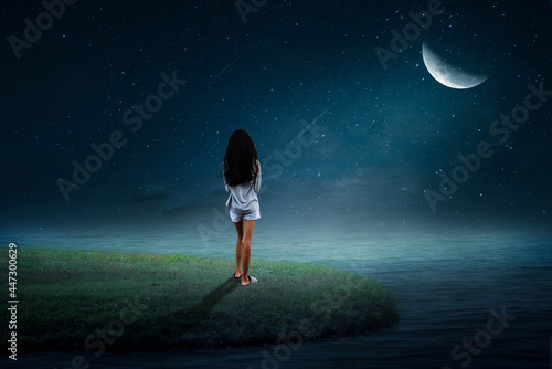 A little girl stood alone on the island in the middle of the sea on the half moon night. photo