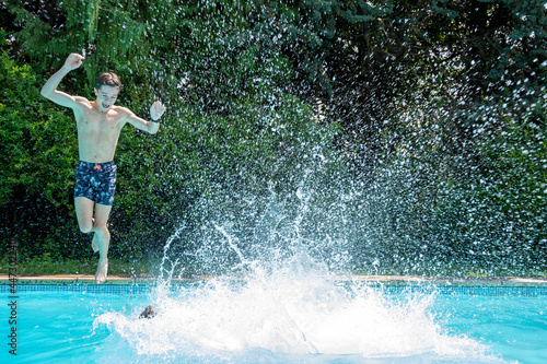 Garçon adolescent au bord d'une piscine sautant dans l'eau avec des éclaboussures