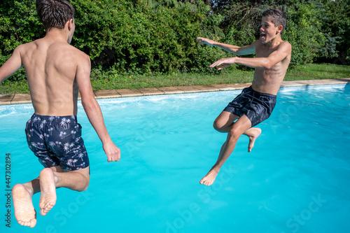 Deux garçons adolescents qui jouent à sauter dans l'eau d'une piscine en extérieur en été photo