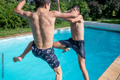 Deux garçons adolescents qui jouent à sauter dans l'eau d'une piscine en extérieur en été