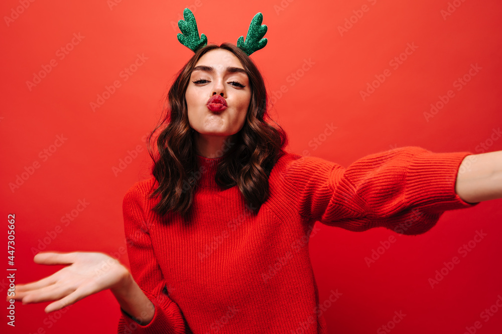 Positive girl with wavy hairstyle blowing kiss on isolated backdrop. Curly lady in bright clothes making selfie on red background.. Positive girl with wavy hairstyle blowing kiss on isolated backdrop. Curly lady in bright clothes making selfie on red background..