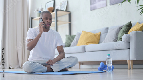 African Man Talking on Phone on Yoga Mat at Home
