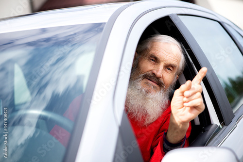 Senior man driver in car. Emotional portrait of an expressive and impulsive mature caucasian male driver with lond beard, showing  his finger in air and shouting to the oncoming car driver photo