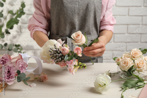 Florist creating beautiful bouquet at white table indoors, closeup