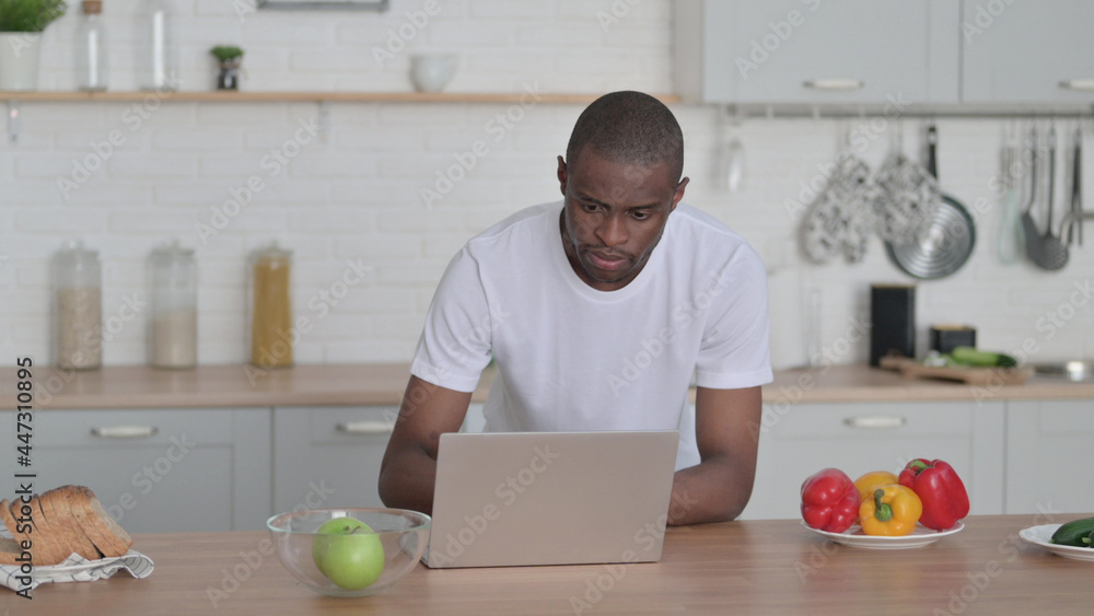 Fototapeta premium African Man Working on Laptop in Kitchen 