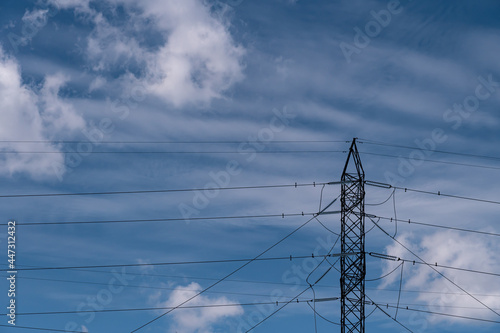 High voltage electric tower transmitter. Industrial transmission power line with blue sky and clouds.