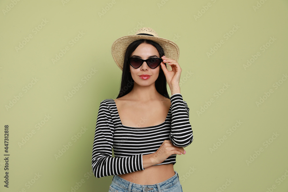 Fototapeta premium Beautiful young woman with straw hat and stylish sunglasses on light green background