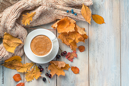 Cozy autumn background with a cup of coffee, a warm sweater and foliage. Top view, copy space.