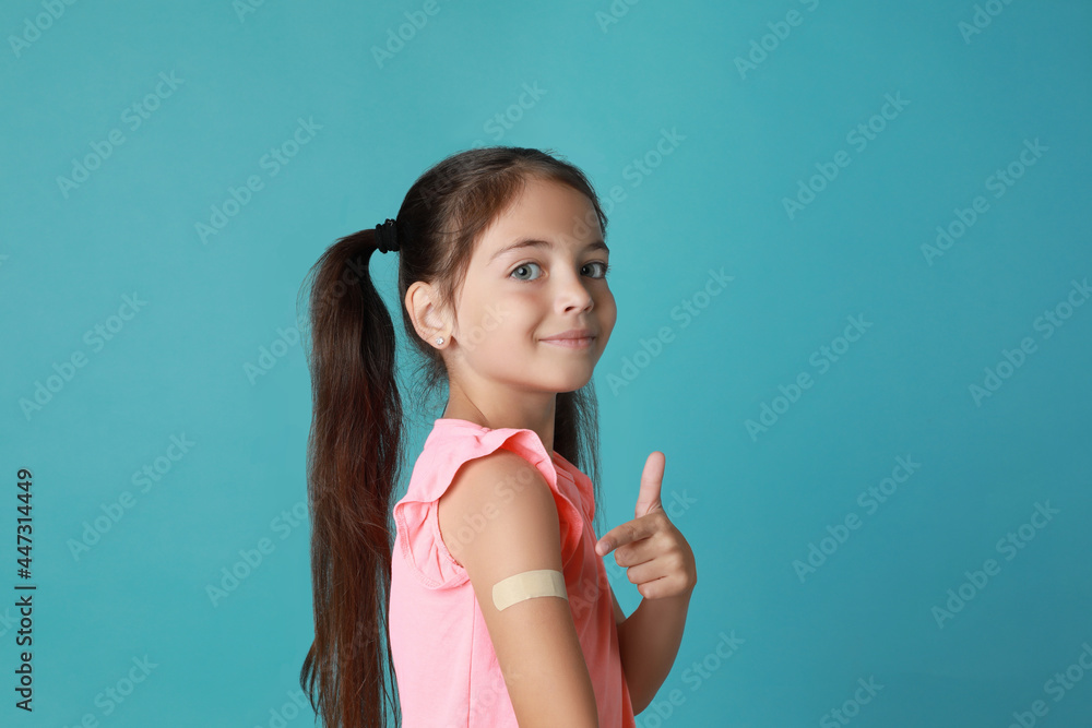Vaccinated little girl showing medical plaster on her arm against light blue background Vaccinated little girl showing medical plaster on her arm against light blue background