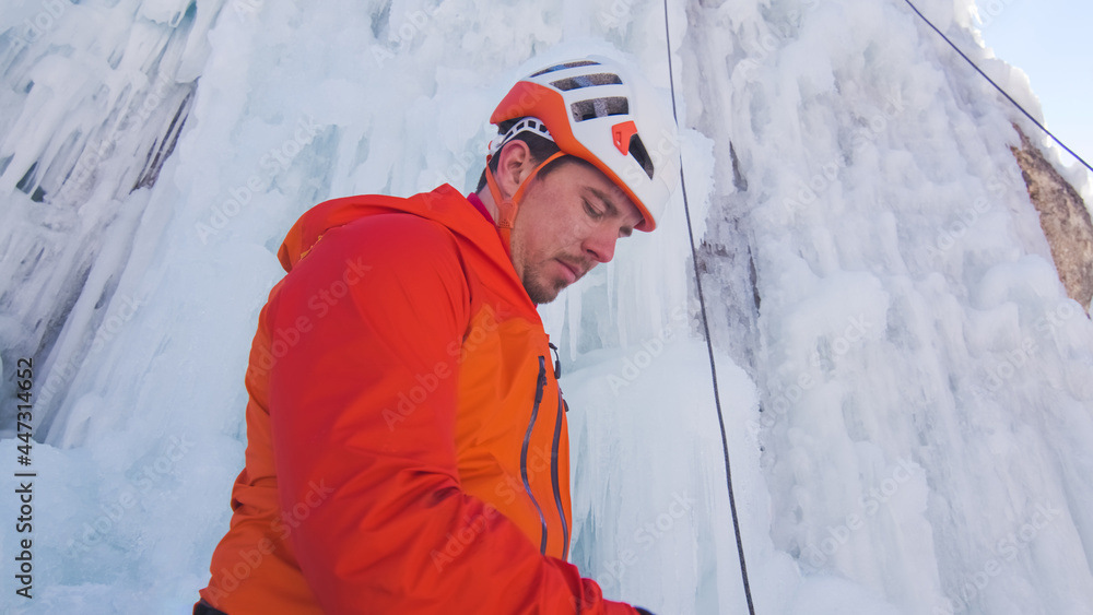 Ice climber, with gloved hands, tying a rope to his harness