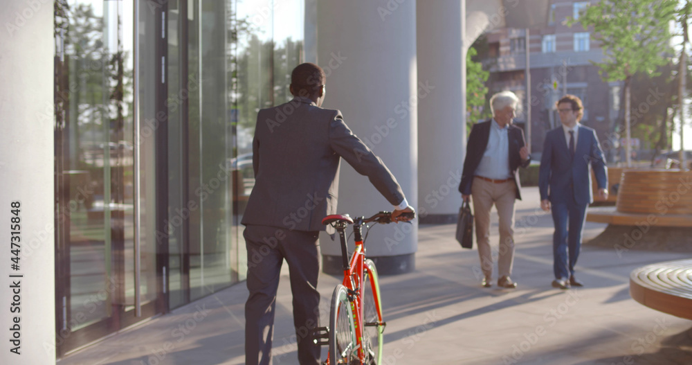 Back view of african businessman with bicycle walking near business center