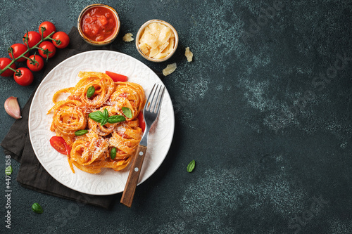 Tasty appetizing classic italian tagliatelle pasta with tomato sauce, cheese parmesan and basil on plate on dark table. View from above, horizontal. Top view with copy space