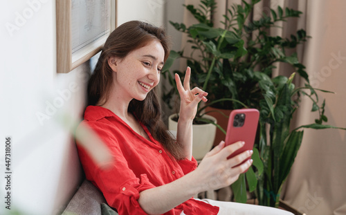 Beautiful young happy woman brunette girl in red blouse sitting at home using smartphone for video chats