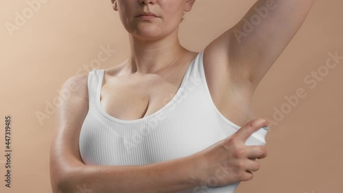 White young lady lift the hand and use antiperspirant to avoid stinking and bad smell. Clean seamless white bra. Studio slow motion video on beige background.