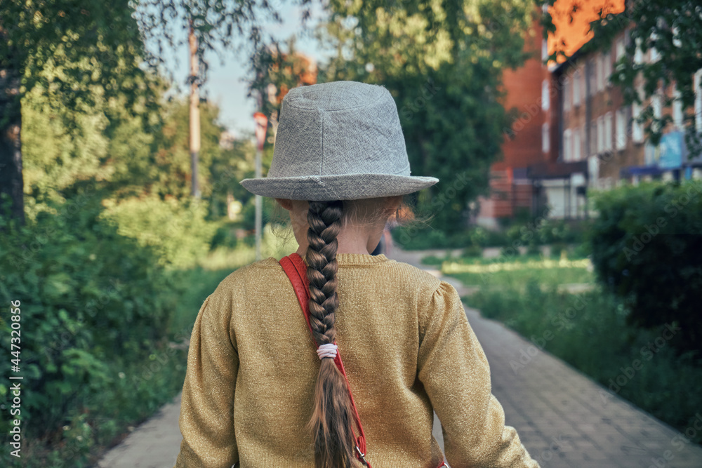 The girl is a child in a yellow shiny jacket and a gray hat, stylish children's clothes. Hair pigtail, ponytail. Walk on the sidewalk