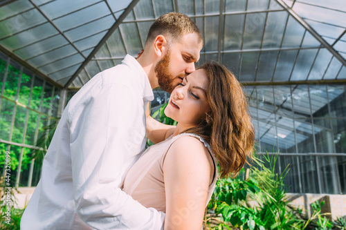 Newlyweds stand in a green botanical garden, a man kisses the bride.