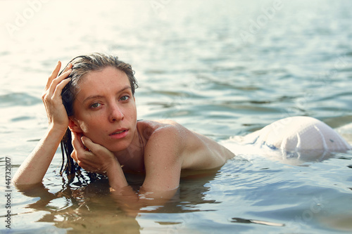Sensual portrait of woman in white dress lying in the water. Summer emotional, beautiful portrait of a swimming woman resting in the water photo