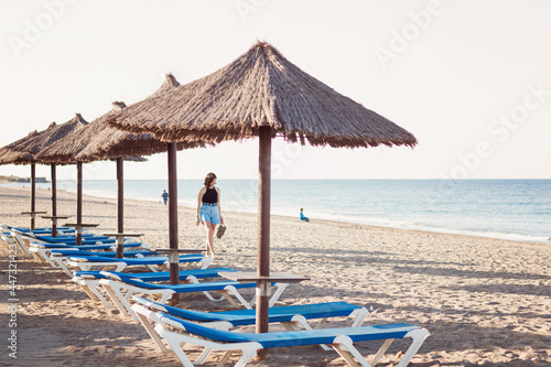 oman walking among natural straw umbrellas next to blue sea