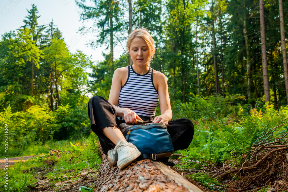 Beautiful blond hair woman sits on log in forest