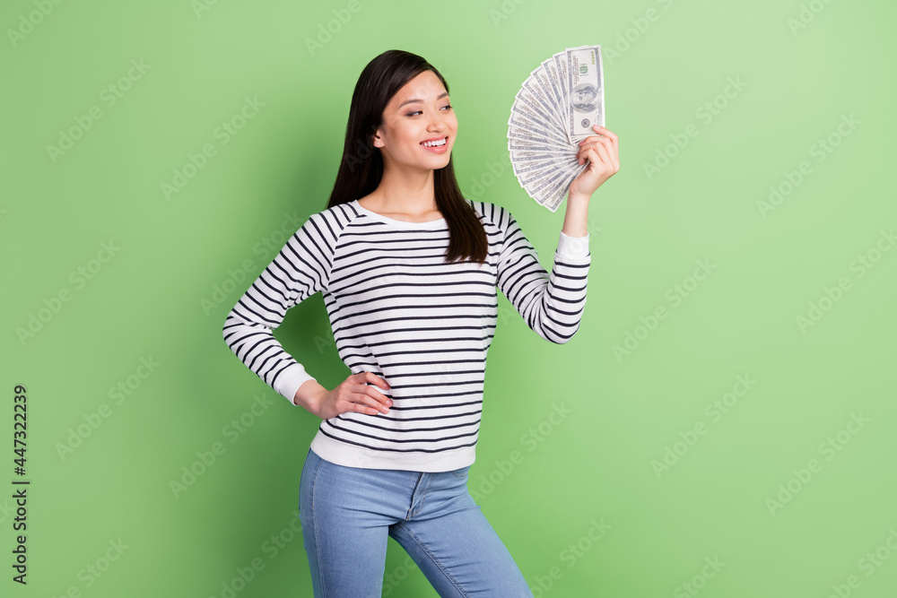 Portrait of attractive trendy cheerful girl holding in hand fan cash spend fund budget isolated over green color background Portrait of attractive trendy cheerful girl holding in hand fan cash spend fund budget isolated over green color background