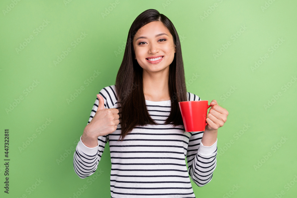 Portrait of attractive cheerful girl drinking beverage showing thumbup deal done yes isolated over green color background Portrait of attractive cheerful girl drinking beverage showing thumbup deal done yes isolated over green color background