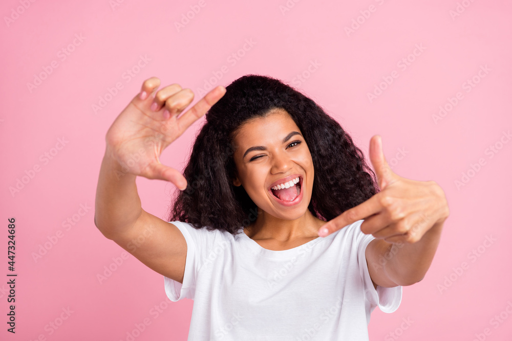 Photo of impressed funky dark skin lady wear white t-shirt smiling winking showing fingers camera shot isolated pink color background Photo of impressed funky dark skin lady wear white t-shirt smiling winking showing fingers camera shot isolated pink color background