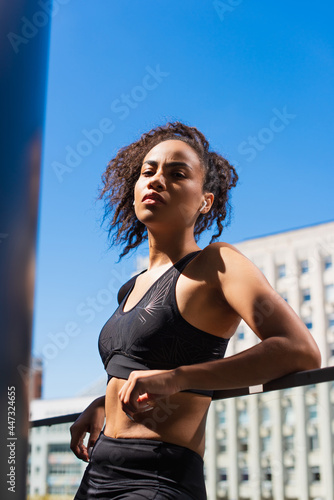 African american woman in earphone and sportswear standing on urban street at daytime © LIGHTFIELD STUDIOS