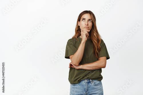 Hmm let me think. Thoughtful adult woman, middle aged mother touch chin, thinking, pondering important decision, looking aside and choosing, standing against white background