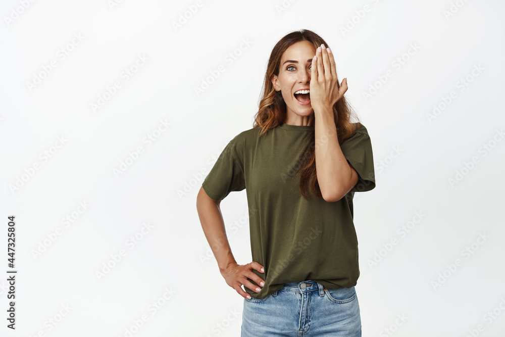 Portrait of woman look surprised with one eye, cover half face with hand and smiling excited, before after cosmetic effect, makeup advertisement, white background Portrait of woman look surprised with one eye, cover half face with hand and smiling excited, before after cosmetic effect, makeup advertisement, white background