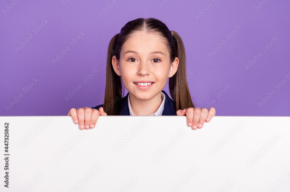 Photo of charming pretty schoolgirl dressed blue uniform smiling holding arms white placard empty space isolated violet color background Photo of charming pretty schoolgirl dressed blue uniform smiling holding arms white placard empty space isolated violet color background