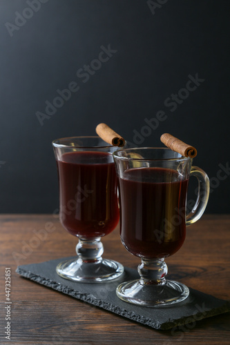 Mulled wine in glass cups with cinnamon and oranges on a wooden table.