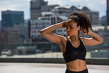 African american sportswoman in earphone stretching arms on urban street