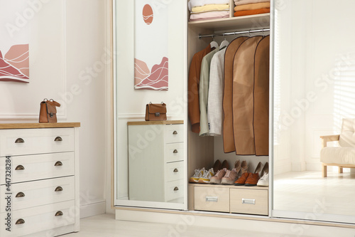 Garment bags with clothes on rack in wardrobe indoors photo