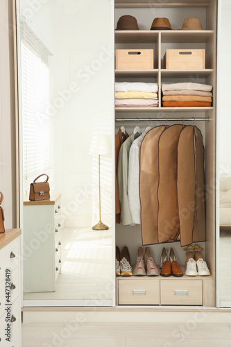 Garment bags with clothes on rack in wardrobe indoors