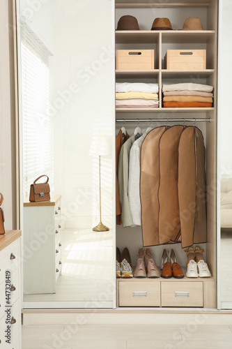 Garment bags with clothes on rack in wardrobe indoors photo