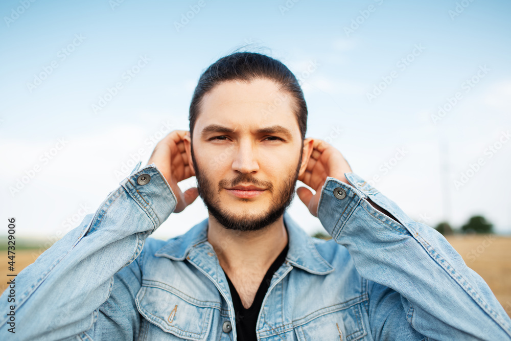 Outdoor portrait of young handsome man, in blue denim jacket, the field.