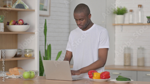 African Man Working on Laptop in Kitchen