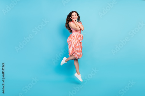 Photo of adorable sweet cheerful lady jump hands cheeks wear striped dress sneakers isolated blue color background