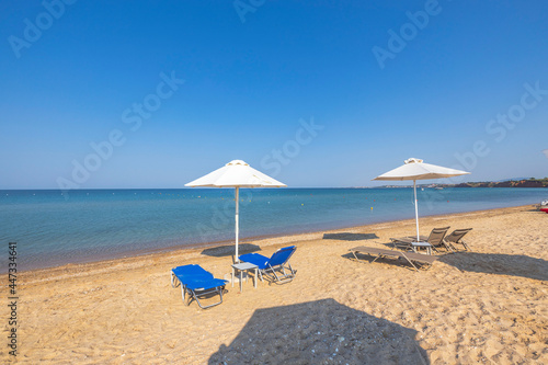 Landscape view of empty sunbeds under umbrellas on sand beach. Greece. 