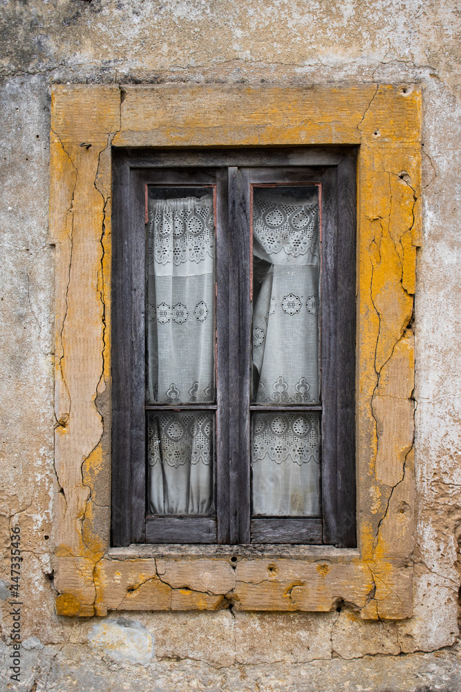 Detail of old window in abandoned rural house with wooden frame and torn lace curtains on a grungy wall with yellow paint border Detail of old window in abandoned rural house with wooden frame and torn lace curtains on a grungy wall with yellow paint border