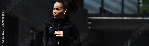 African american woman in earphone jogging outdoors, banner