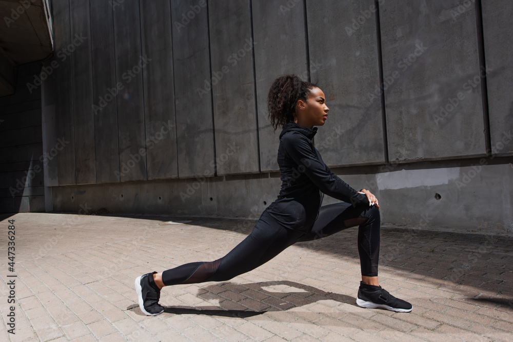 Fototapeta premium Side view of african american sportswoman stretching outdoors